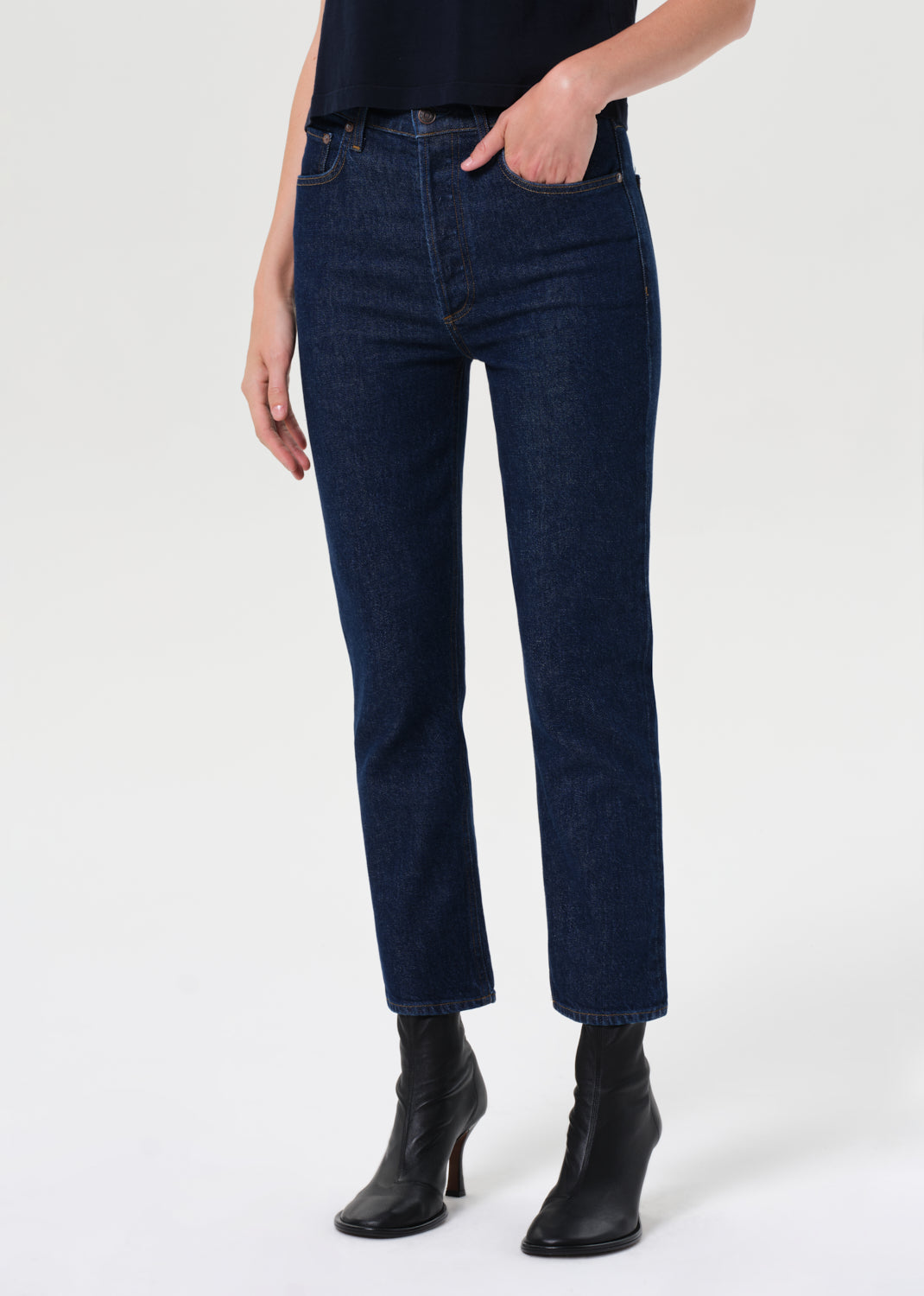 Person wearing dark blue jeans and black boots on a white background