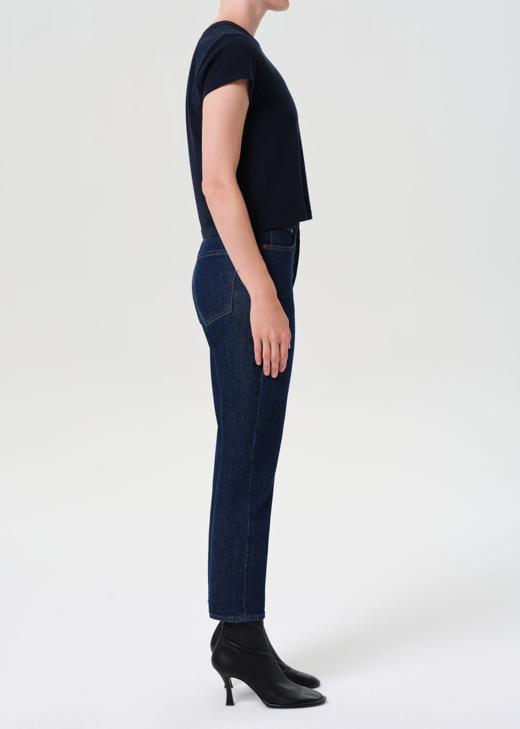 Person wearing dark blue jeans and black shoes on a white background