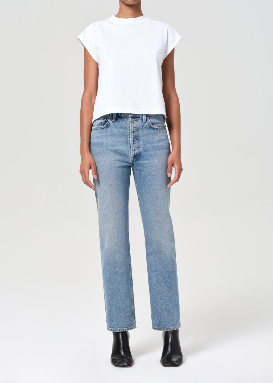 Person wearing light blue jeans and a white top on a white background
