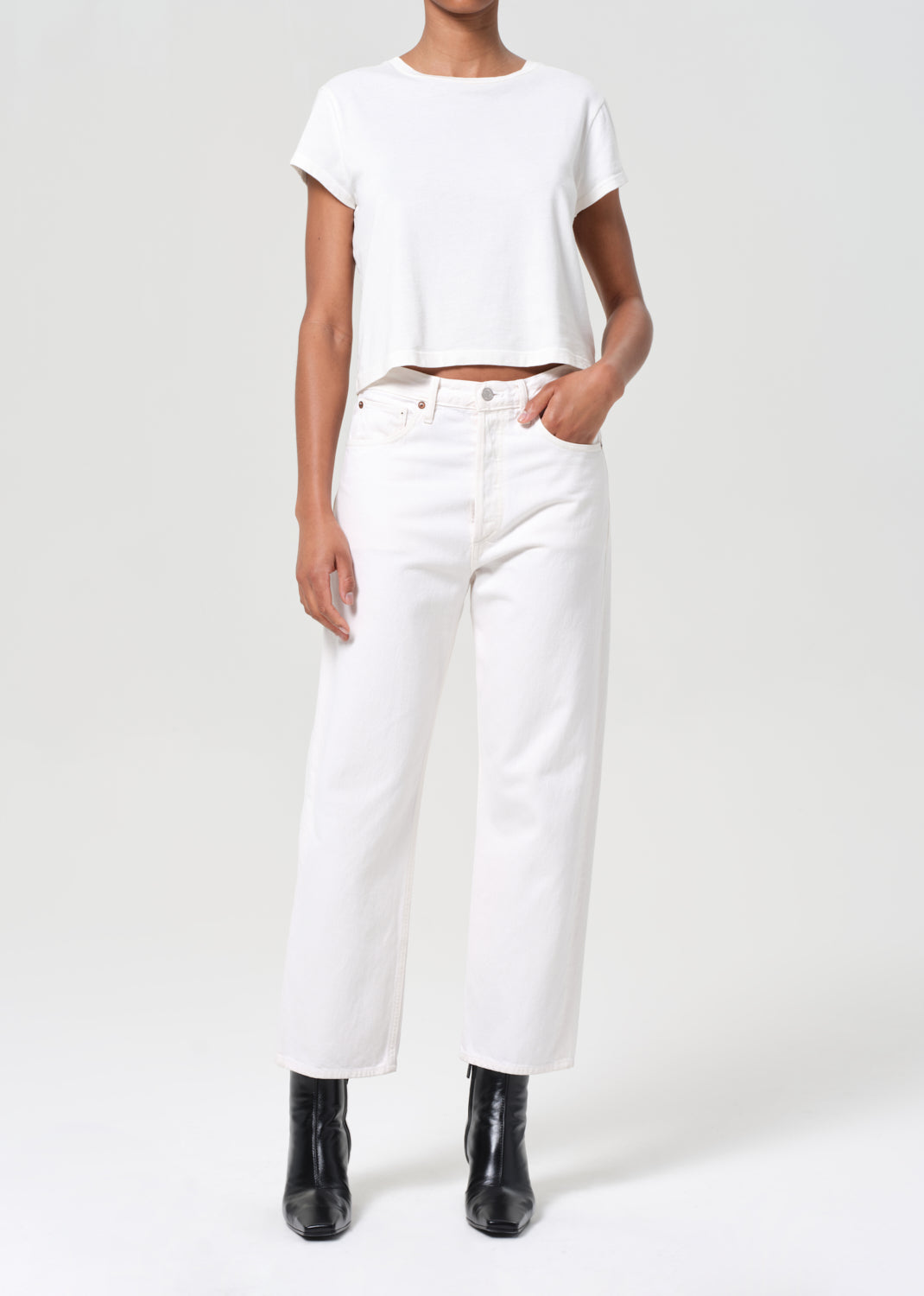 Person wearing a white t-shirt and white pants with black boots on a white background