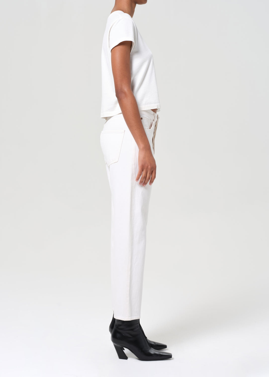 Person wearing a white t-shirt and pants with black shoes on a plain background