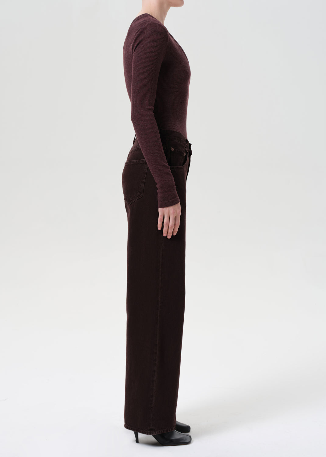 Person wearing a brown long-sleeve top and dark pants on a white background