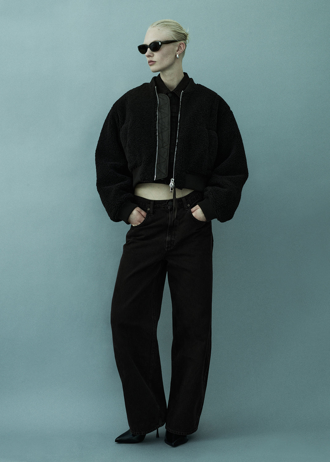 Person wearing a black outfit with sunglasses on a light blue background