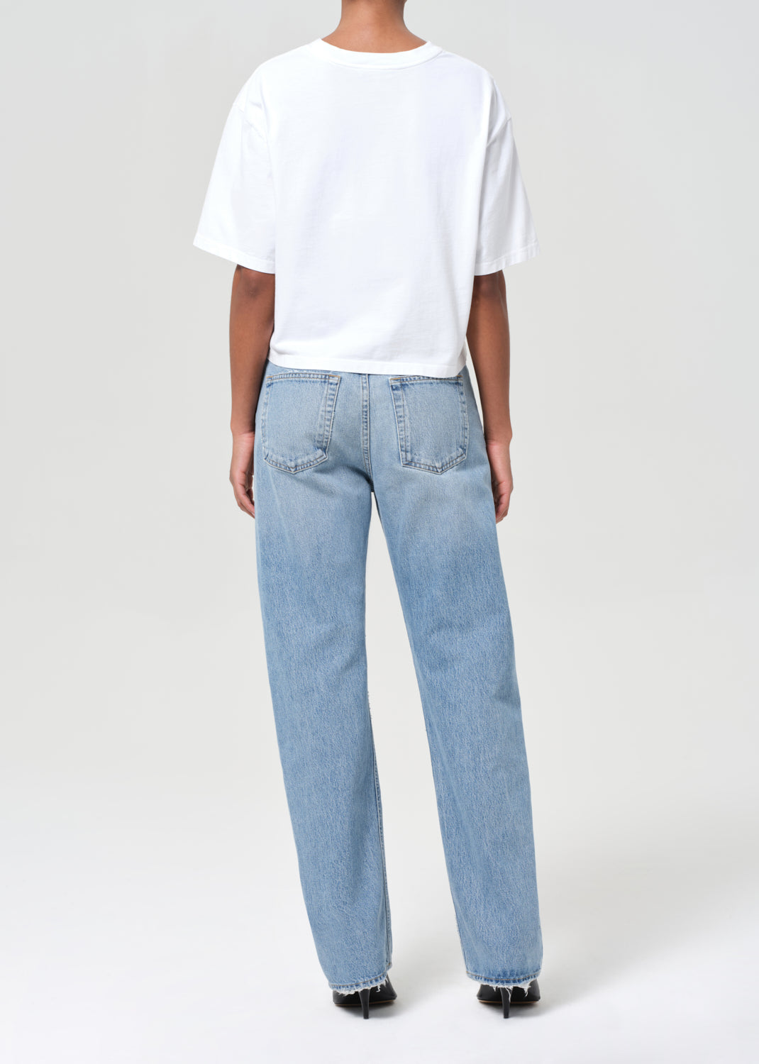 Person wearing a white t-shirt and light blue jeans on a plain background