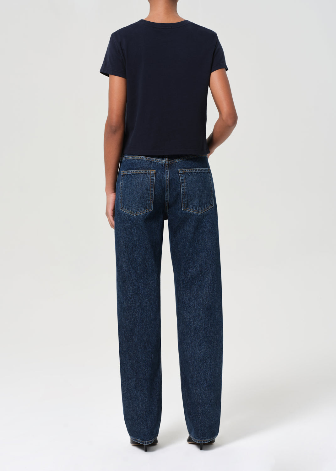 Person wearing a navy t-shirt and dark blue jeans on a white background