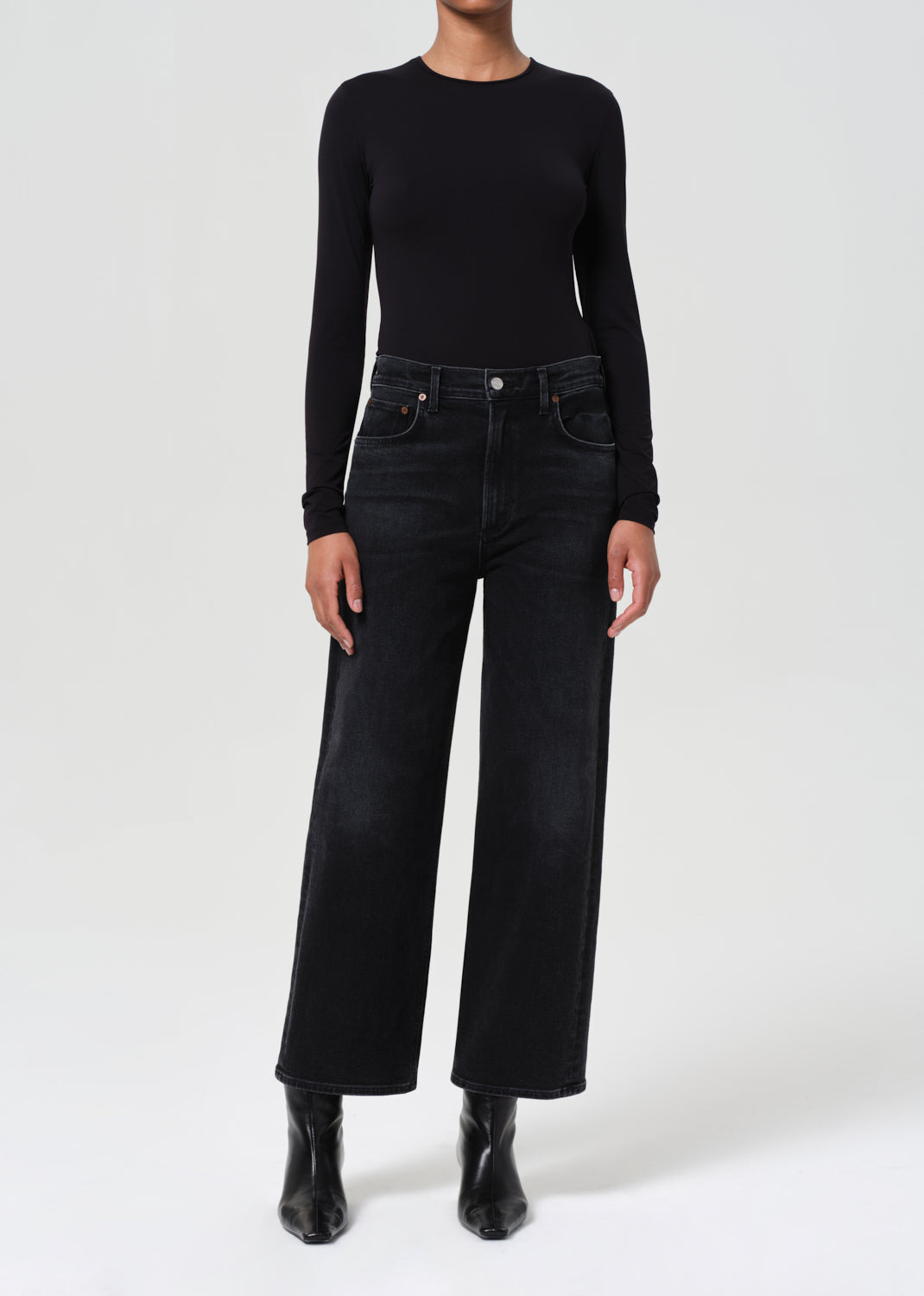 Person wearing a black long-sleeve top and black wide-leg jeans on a white background