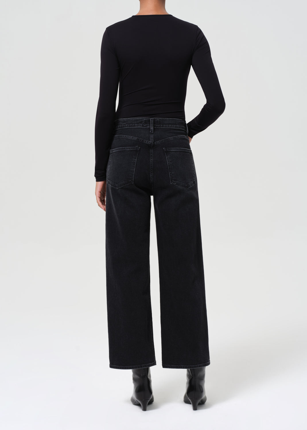 Person wearing black high-waisted jeans and a black long-sleeve top on a white background