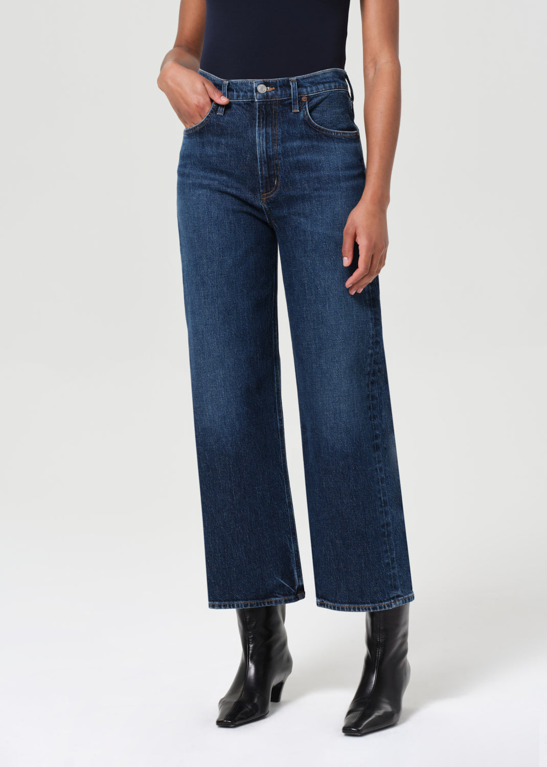 Person wearing dark blue jeans and black boots on a white background