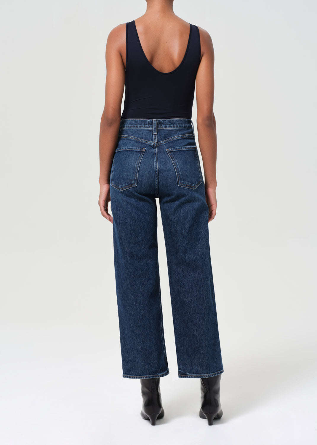 Person wearing blue jeans and a black tank top on a white background