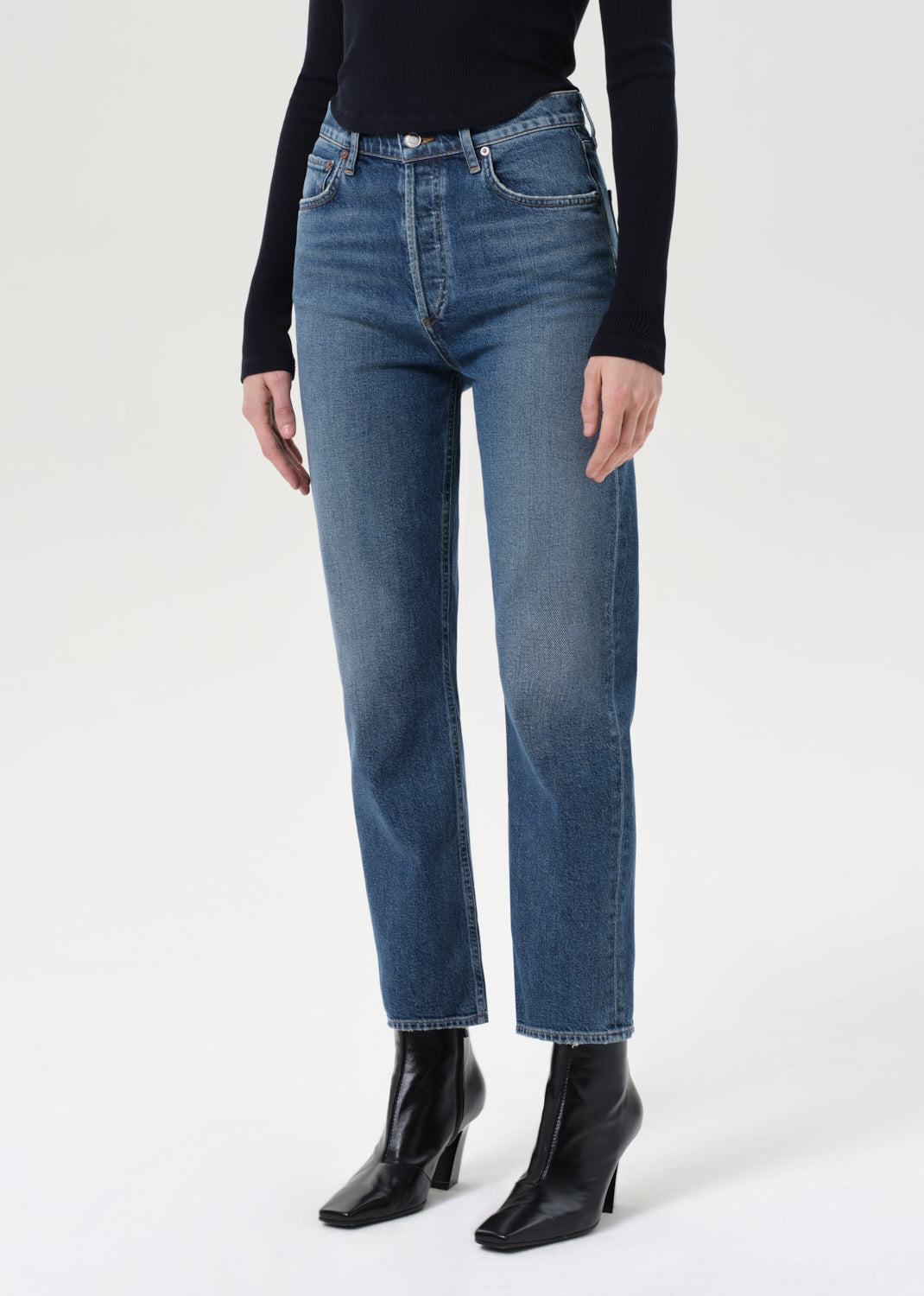 Person wearing blue jeans and black boots on a white background