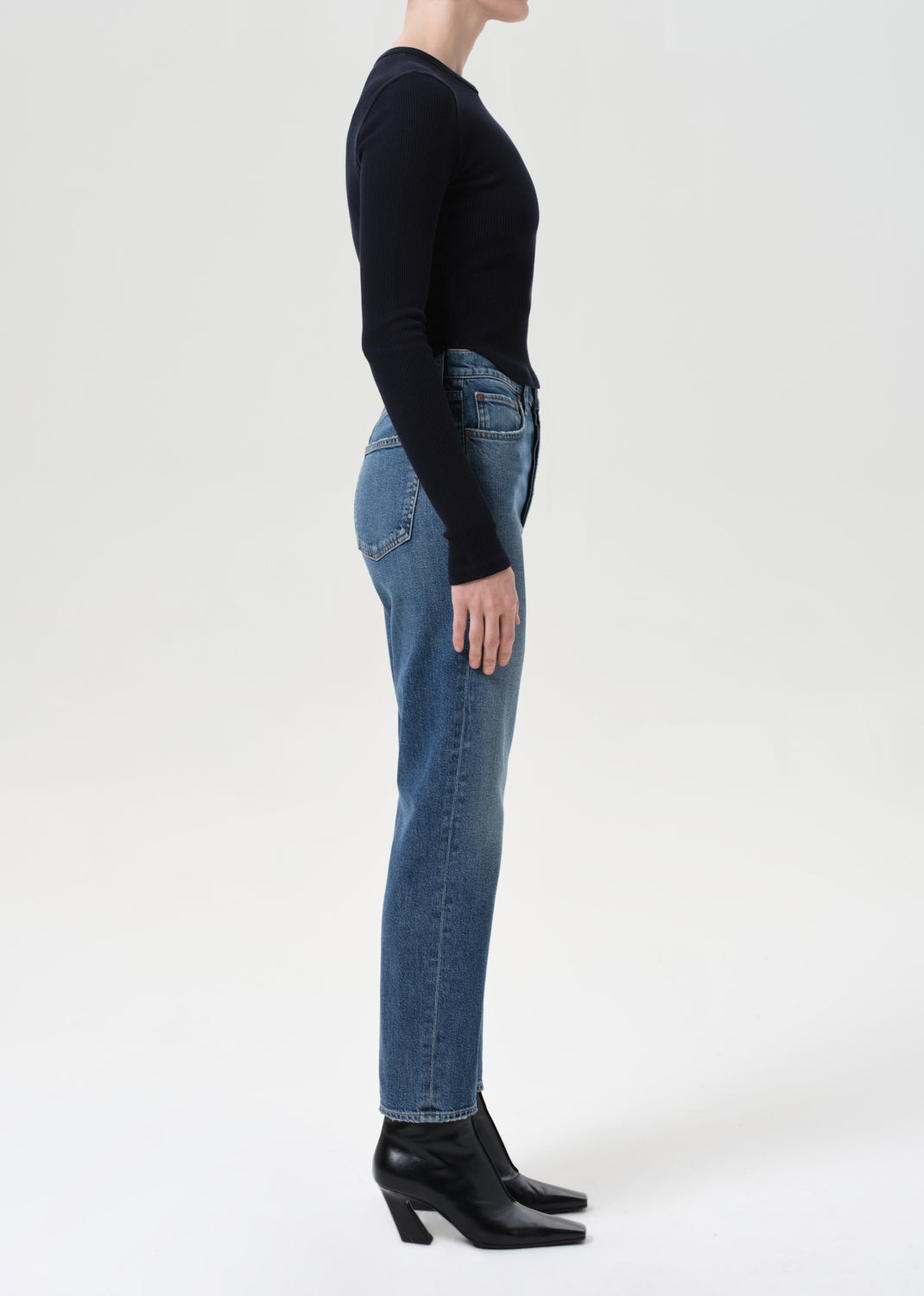 Person wearing a black long-sleeve top and blue jeans on a white background
