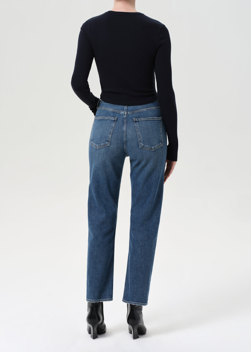 Person wearing blue jeans and a black top on a white background