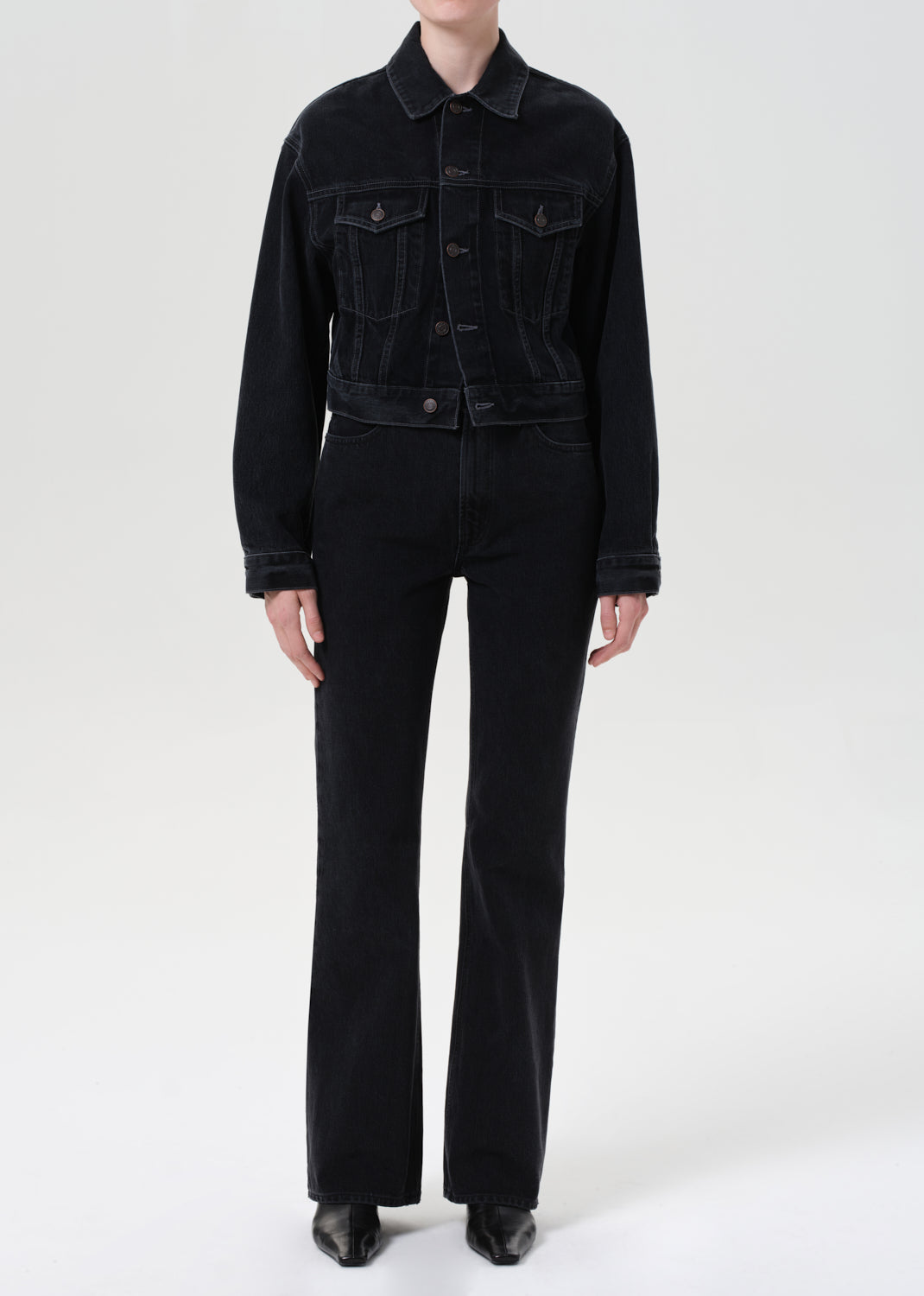 Person wearing a black denim jacket and pants on a white background