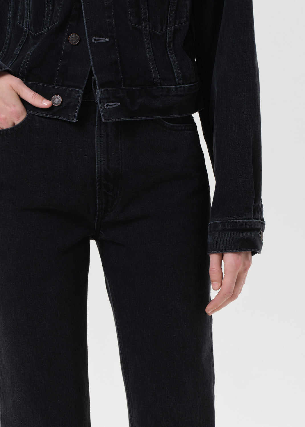 Person wearing a black denim jacket and black jeans on a white background