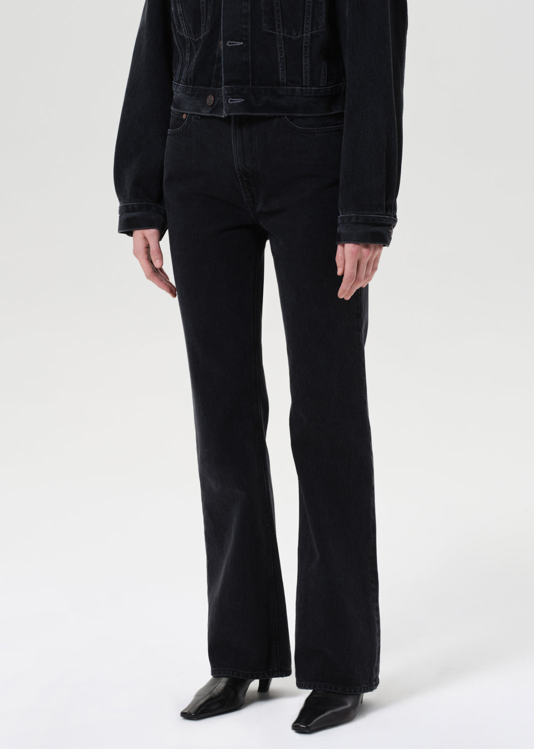 Person wearing black flared jeans and a black jacket on a white background