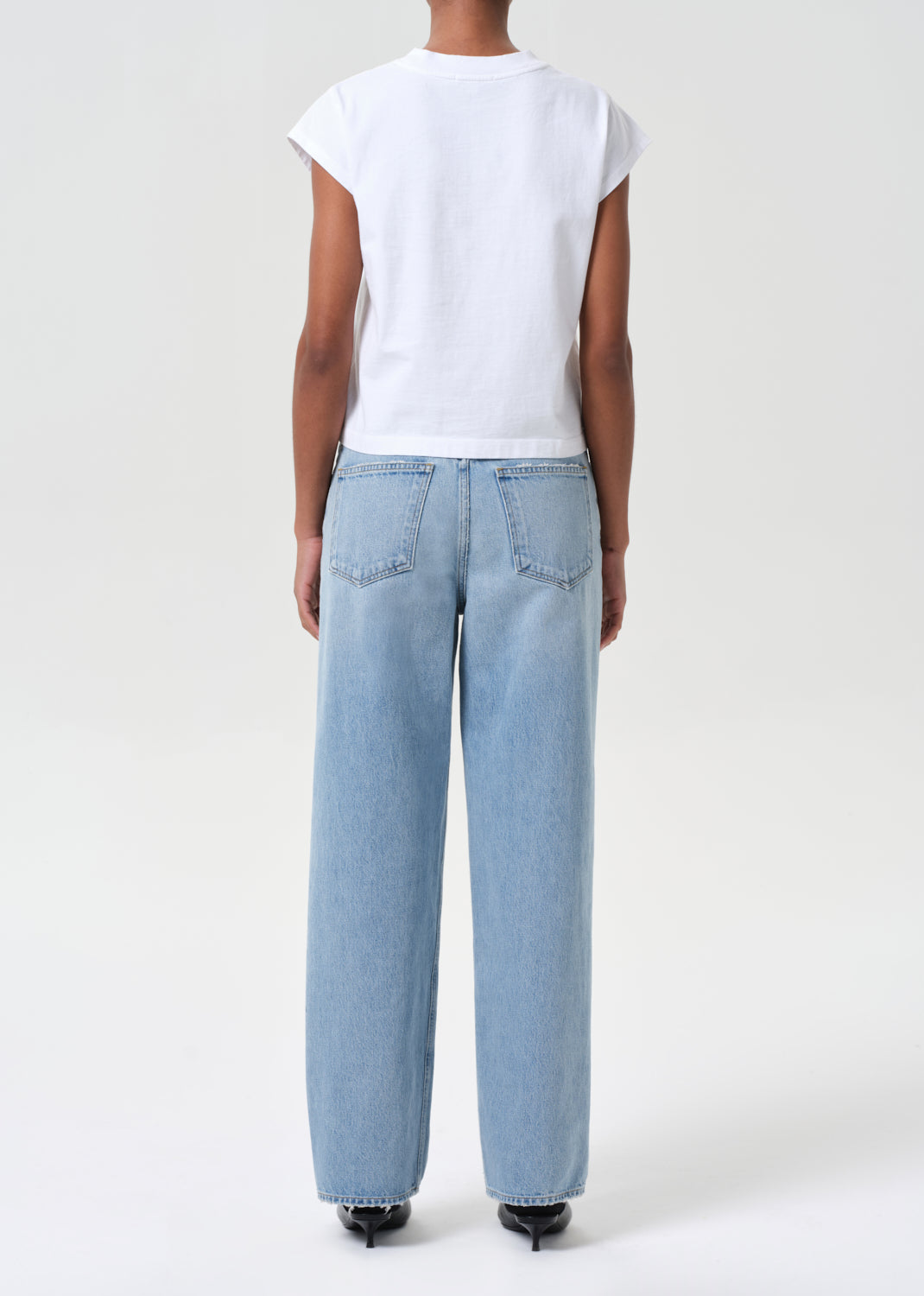 Person wearing light blue jeans and a white top on a white background