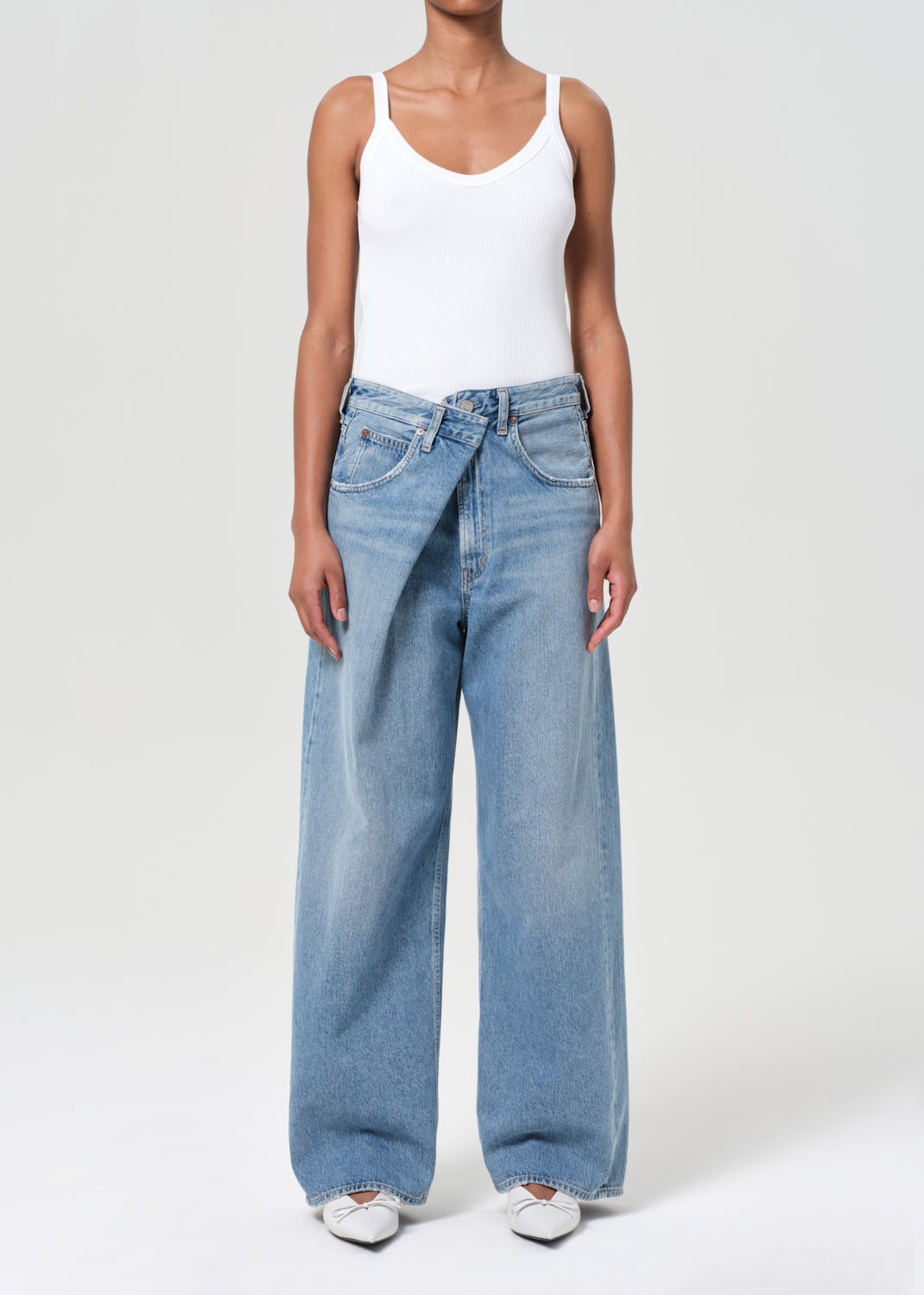 Person wearing a white tank top and blue jeans on a white background