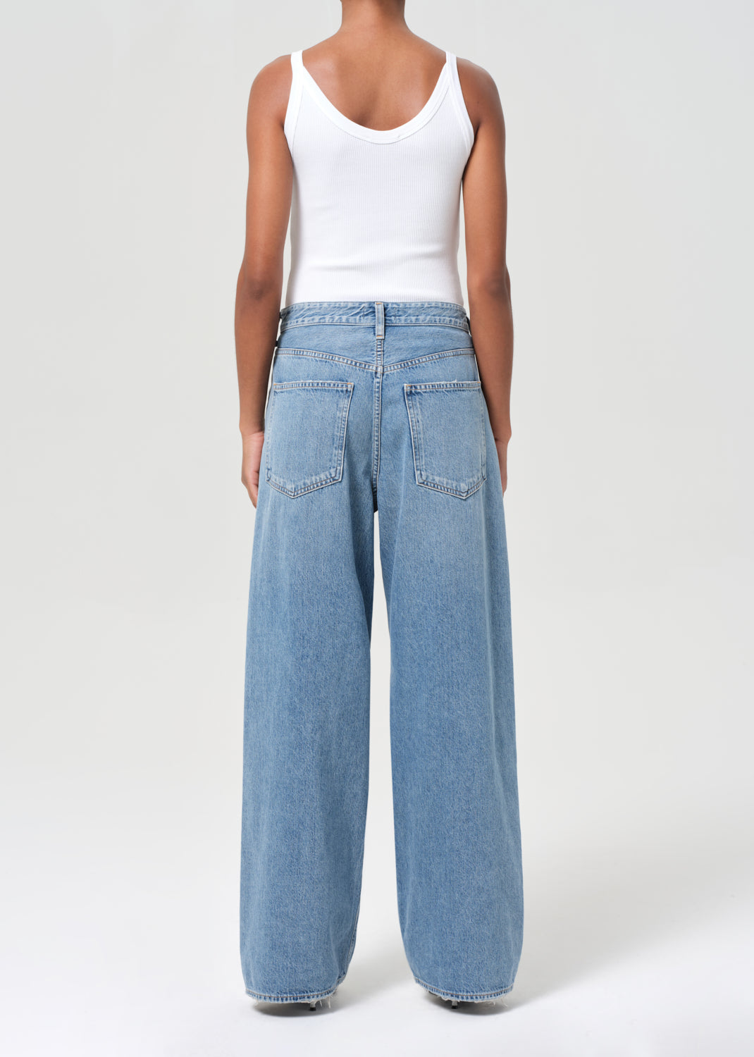 Person wearing light blue jeans and a white tank top on a white background