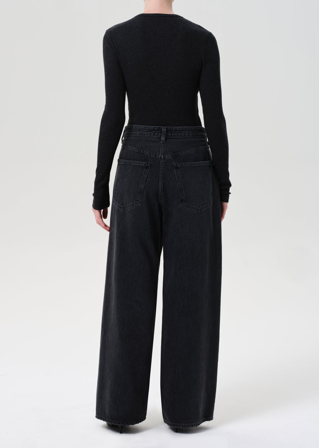Person wearing a black long-sleeve top and wide-leg black jeans on a white background