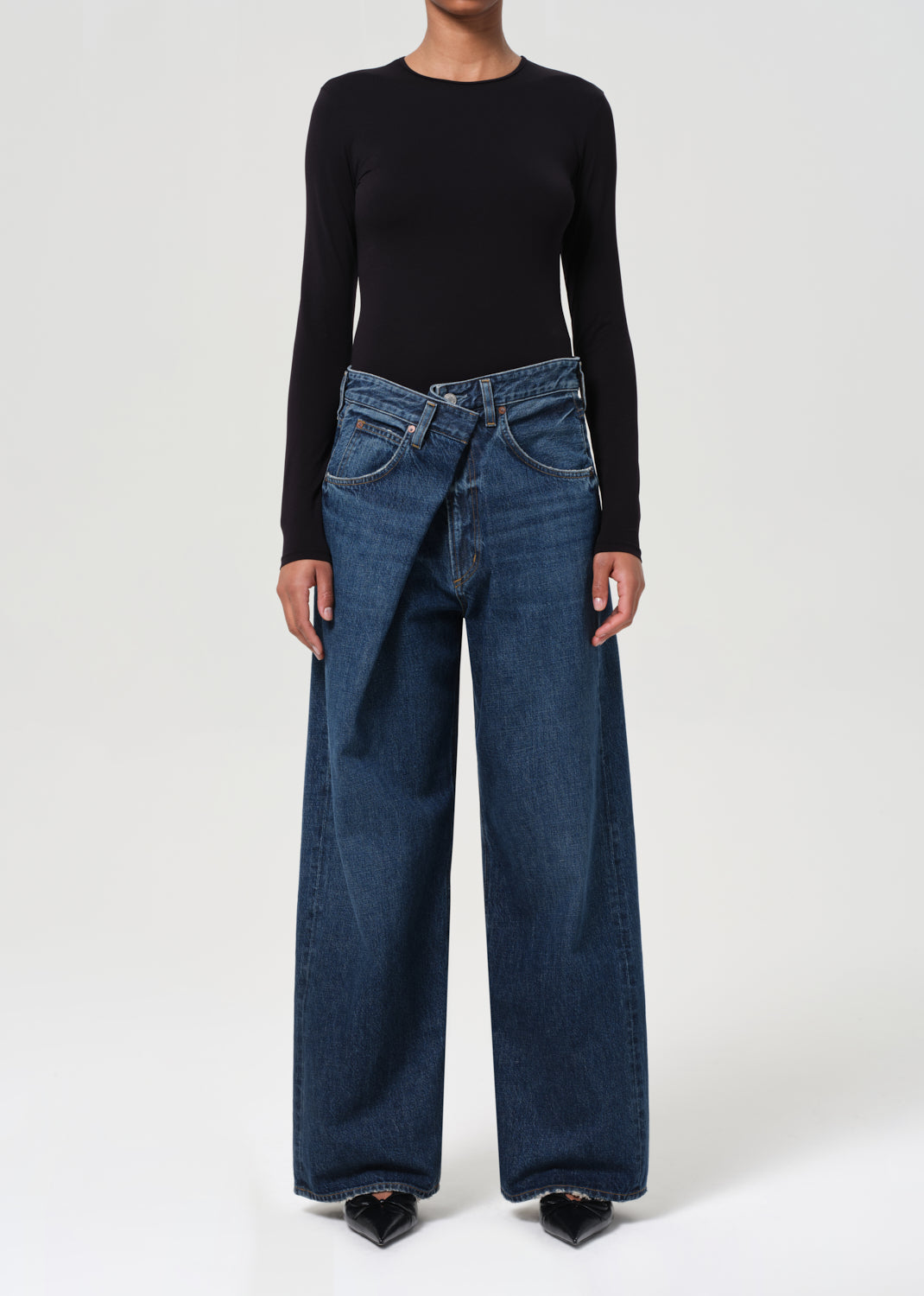 Person wearing a black long-sleeve top and blue wide-leg jeans on a white background