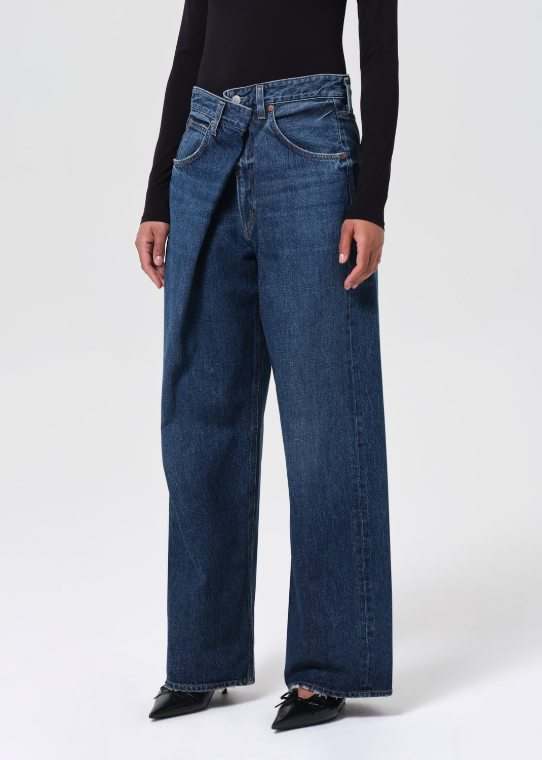 Person wearing blue jeans and a black top on a white background