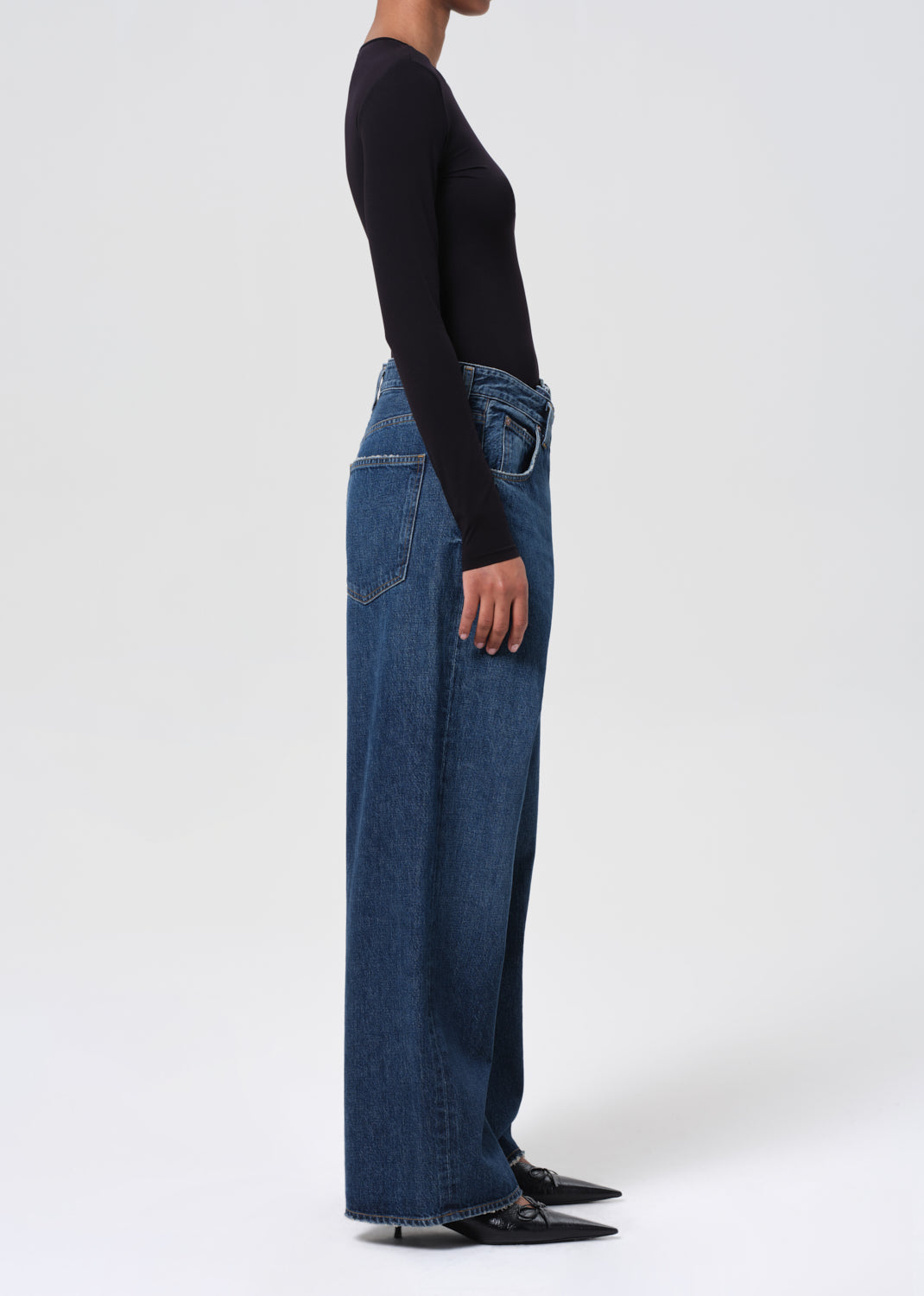 Person wearing blue jeans and a black top on a white background