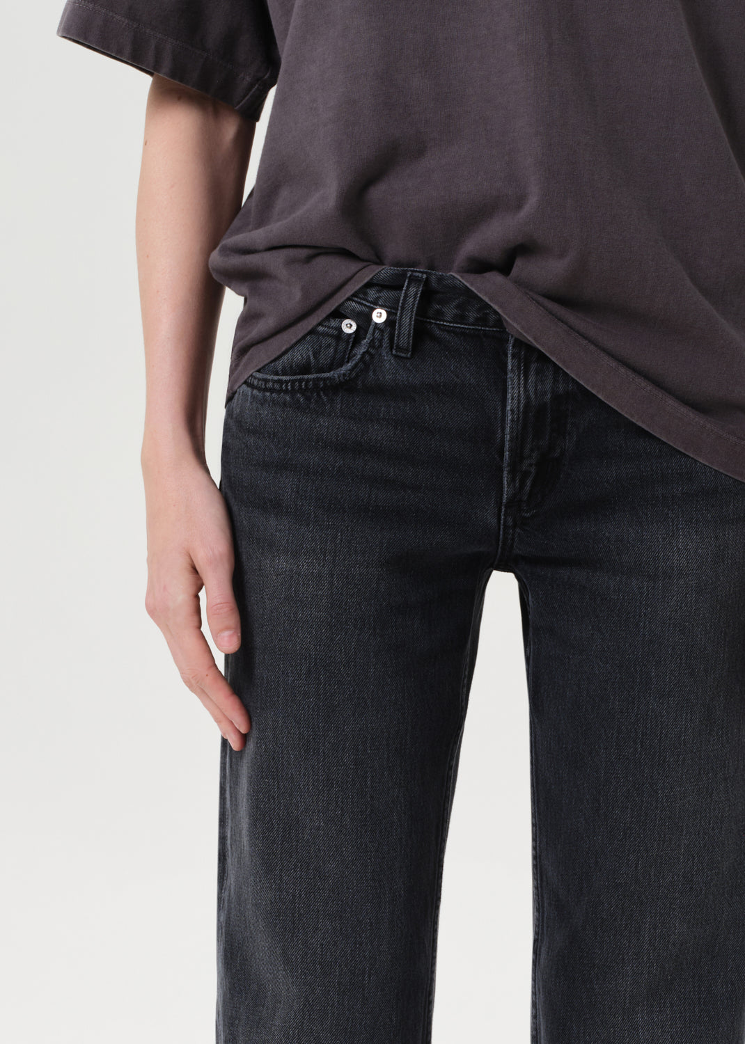 Person wearing a dark gray t-shirt and black jeans on a light gray background