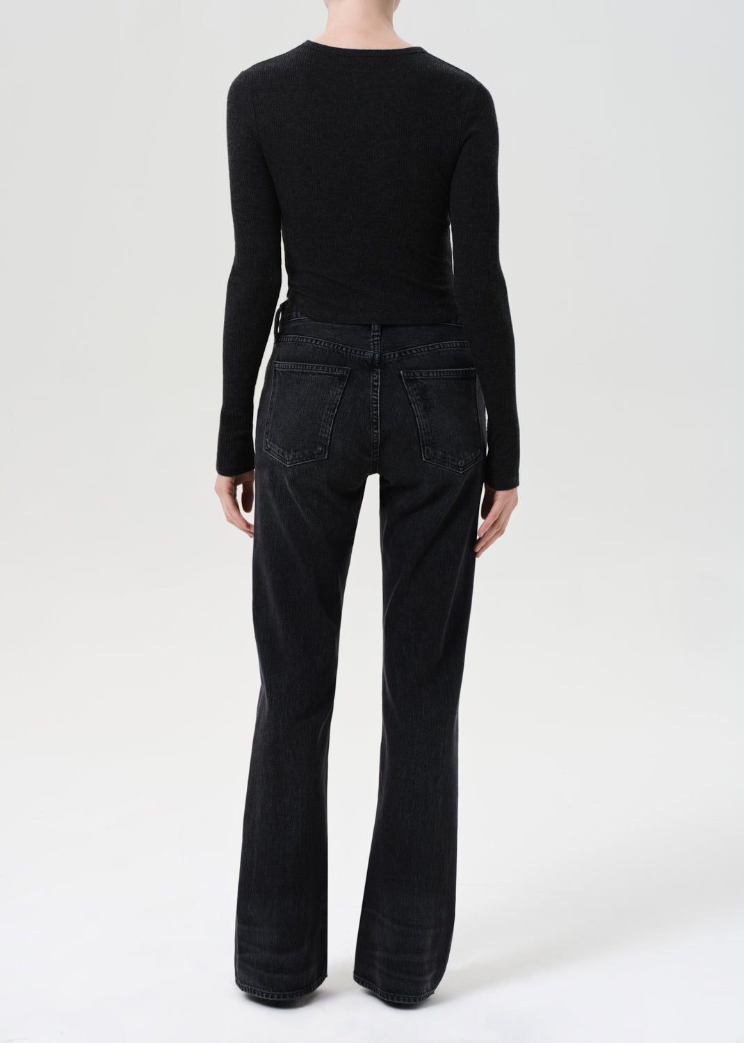 Person wearing a black long-sleeve top and black flared jeans on a white background