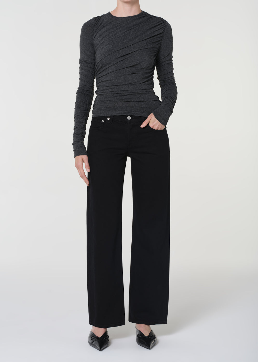 Person wearing a black ruched top and black pants on a white background