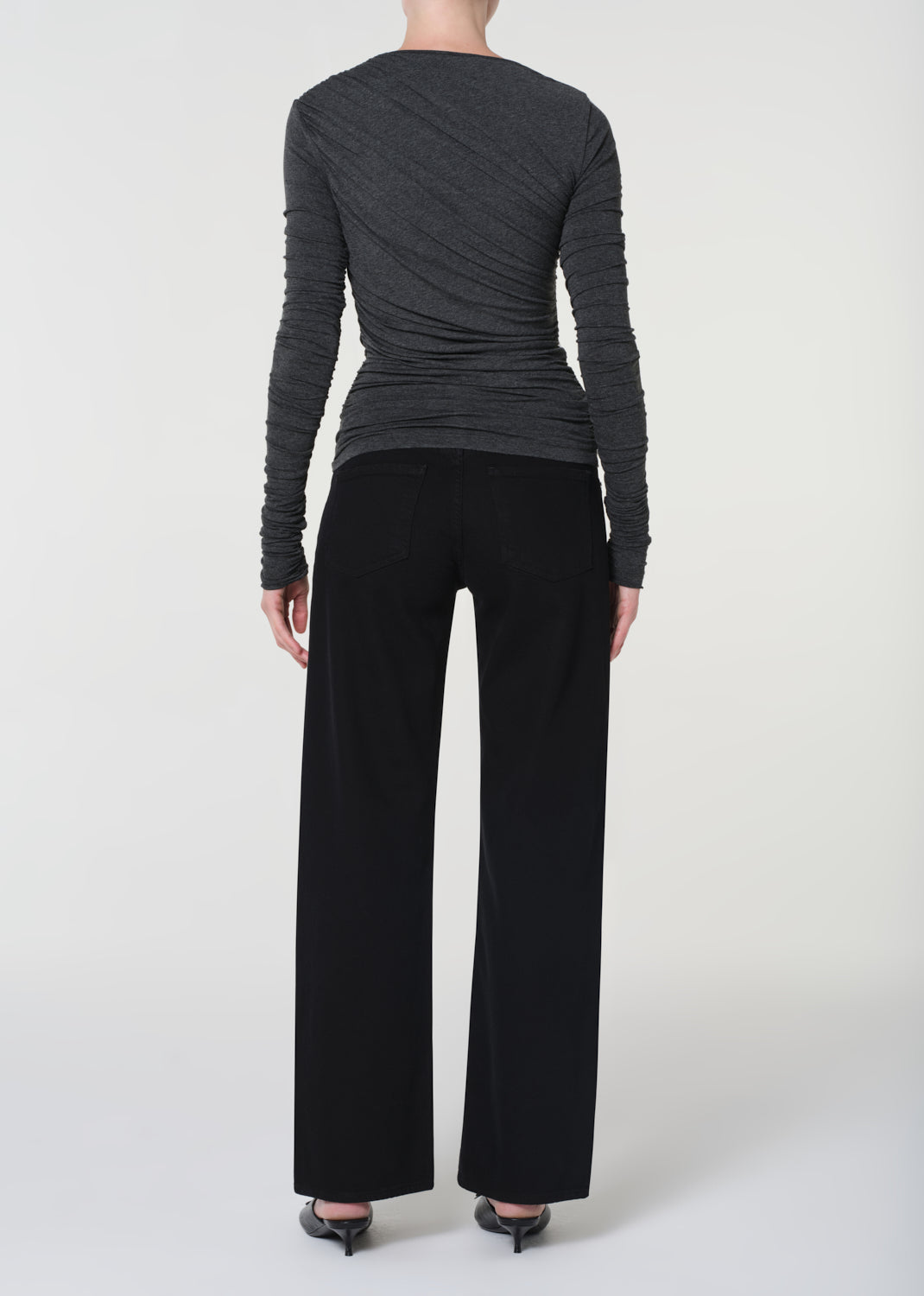 Person wearing a gray long-sleeve top and black pants on a white background