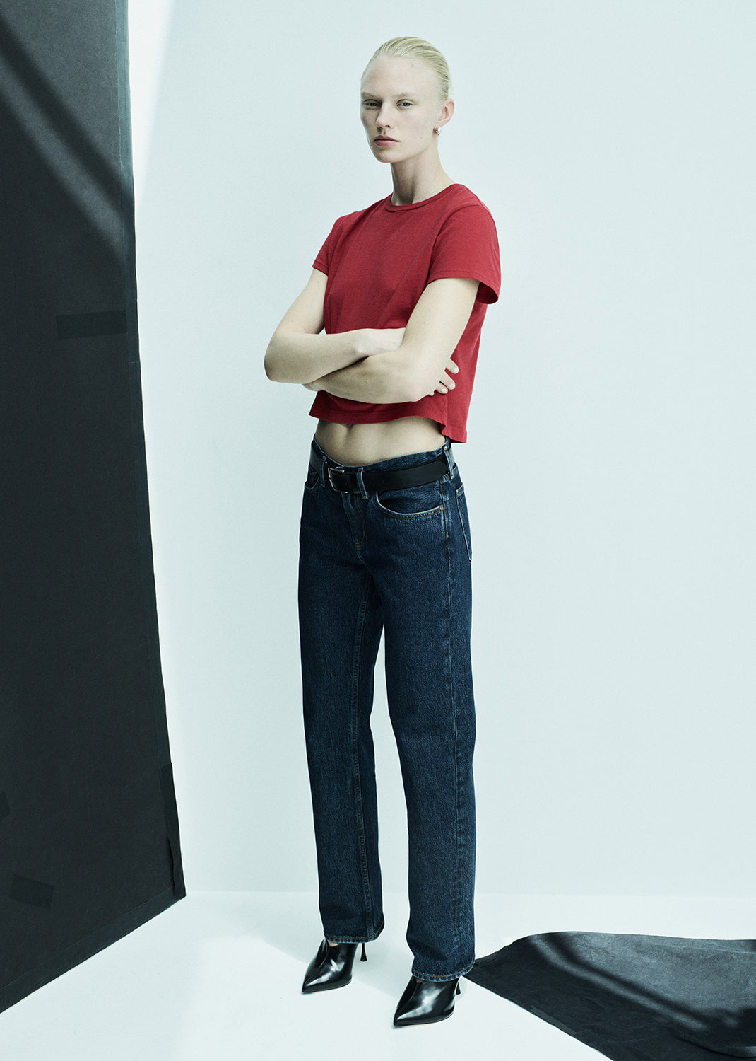 Person wearing a red shirt and blue jeans standing against a white background