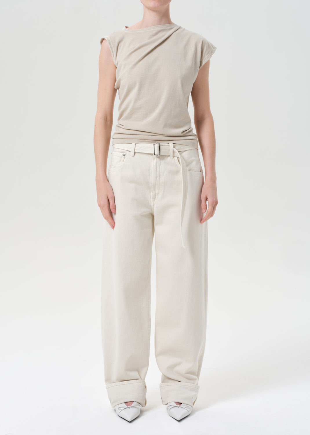 Person wearing a beige top and white pants on a white background
