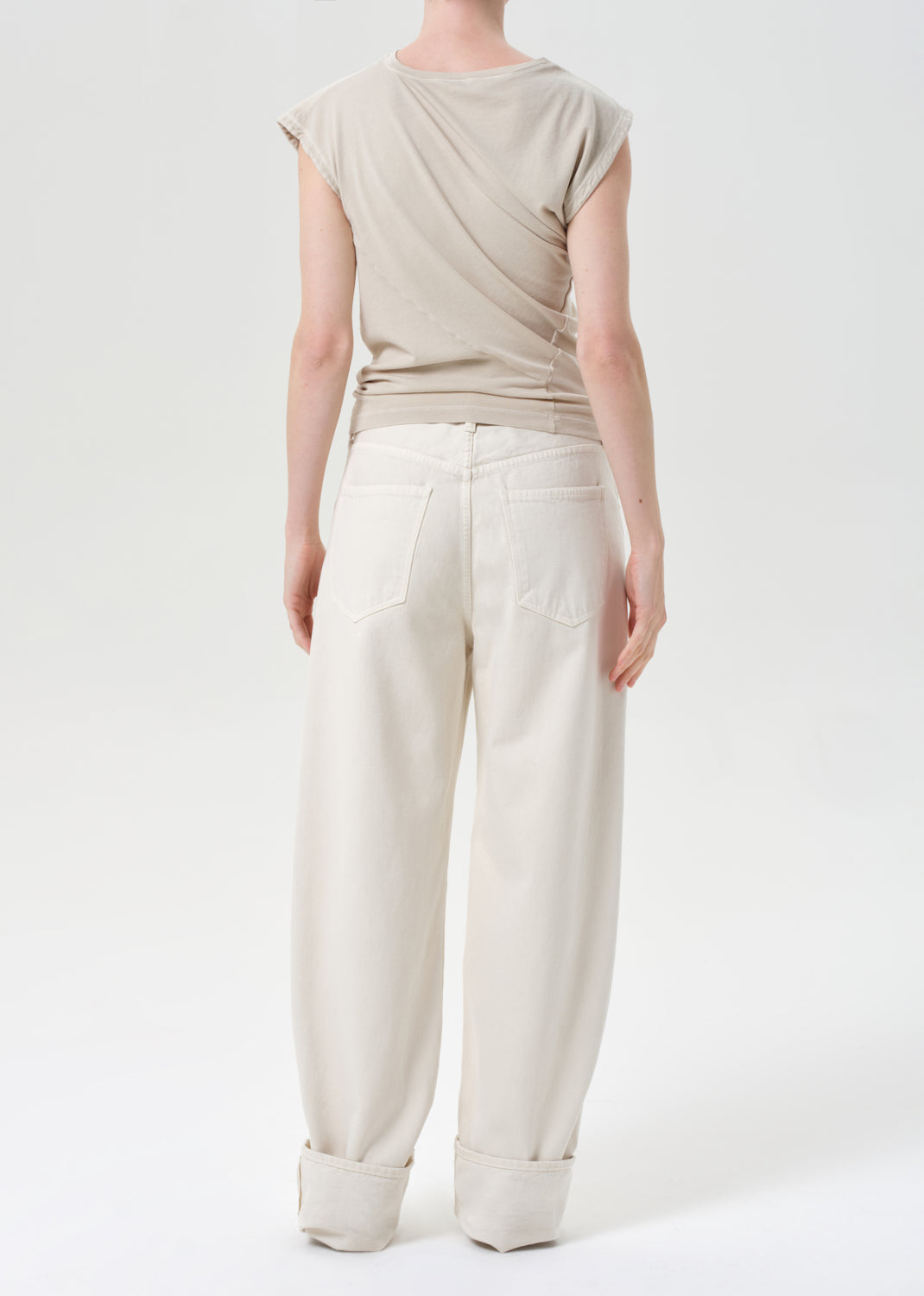 Person wearing a beige top and white pants on a white background