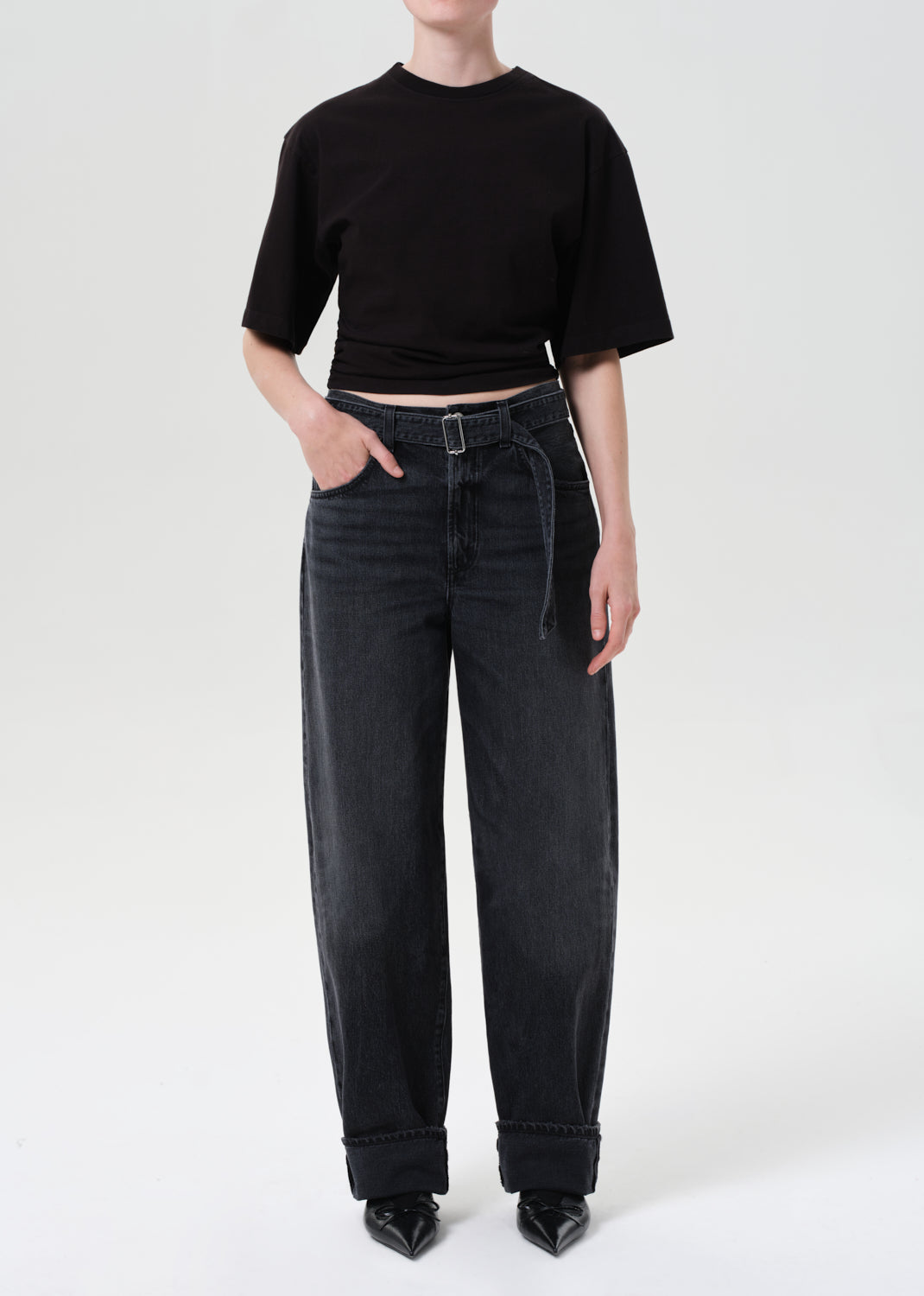 Person wearing a black cropped t-shirt and black high-waisted jeans on a white background
