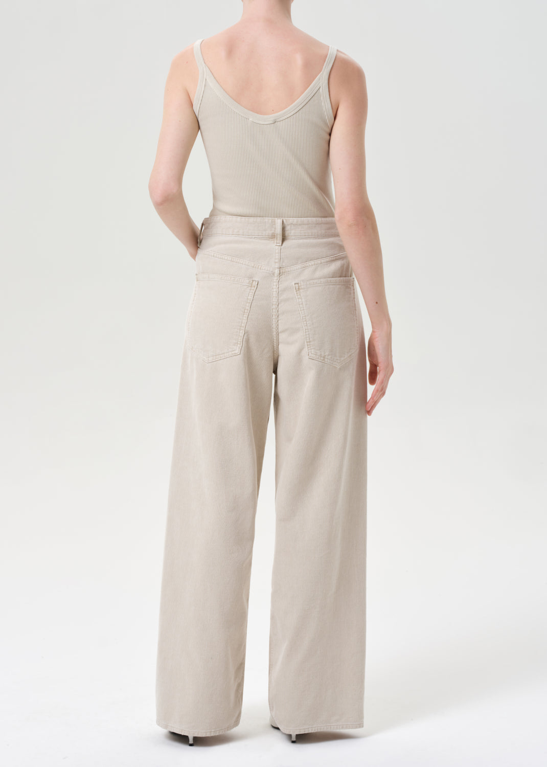 Person wearing a beige sleeveless top and wide-leg pants on a white background
