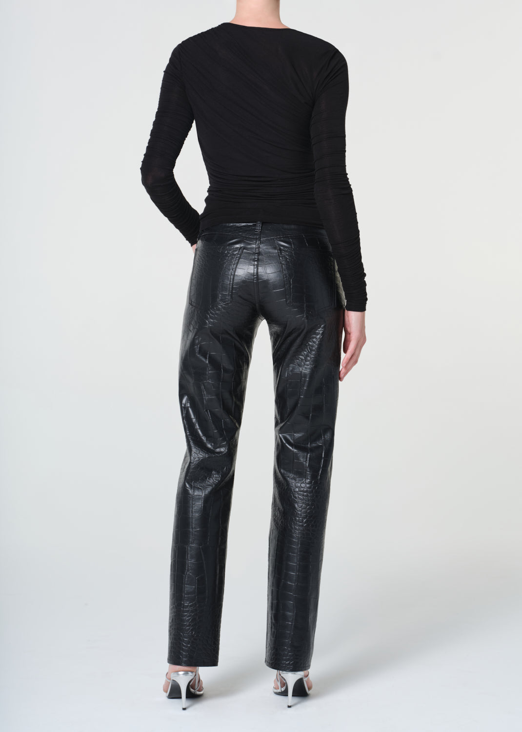Person wearing black long-sleeve top and shiny black pants on a white background