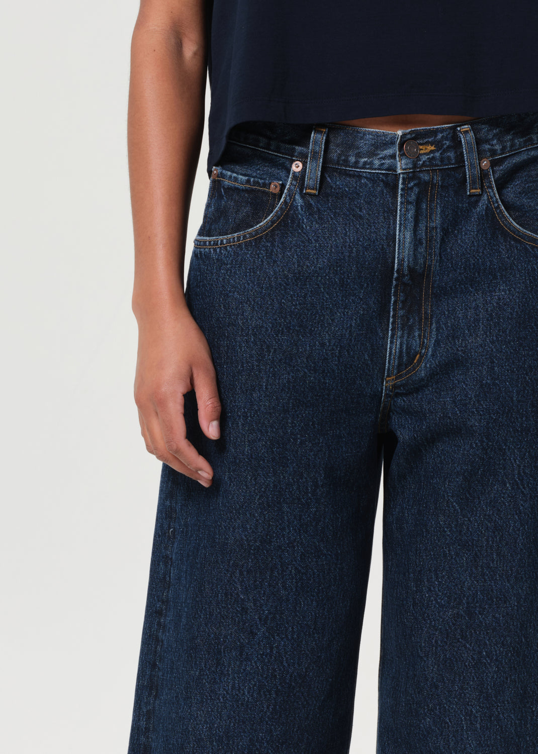 Person wearing dark blue jeans on a plain background