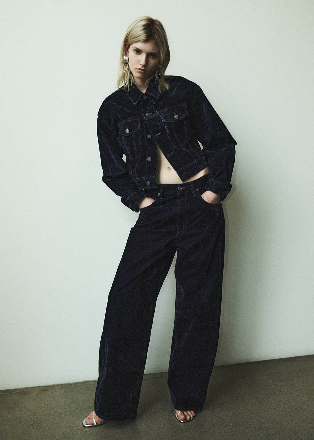 Person wearing a black denim jacket and blue velvet pants against a white wall.