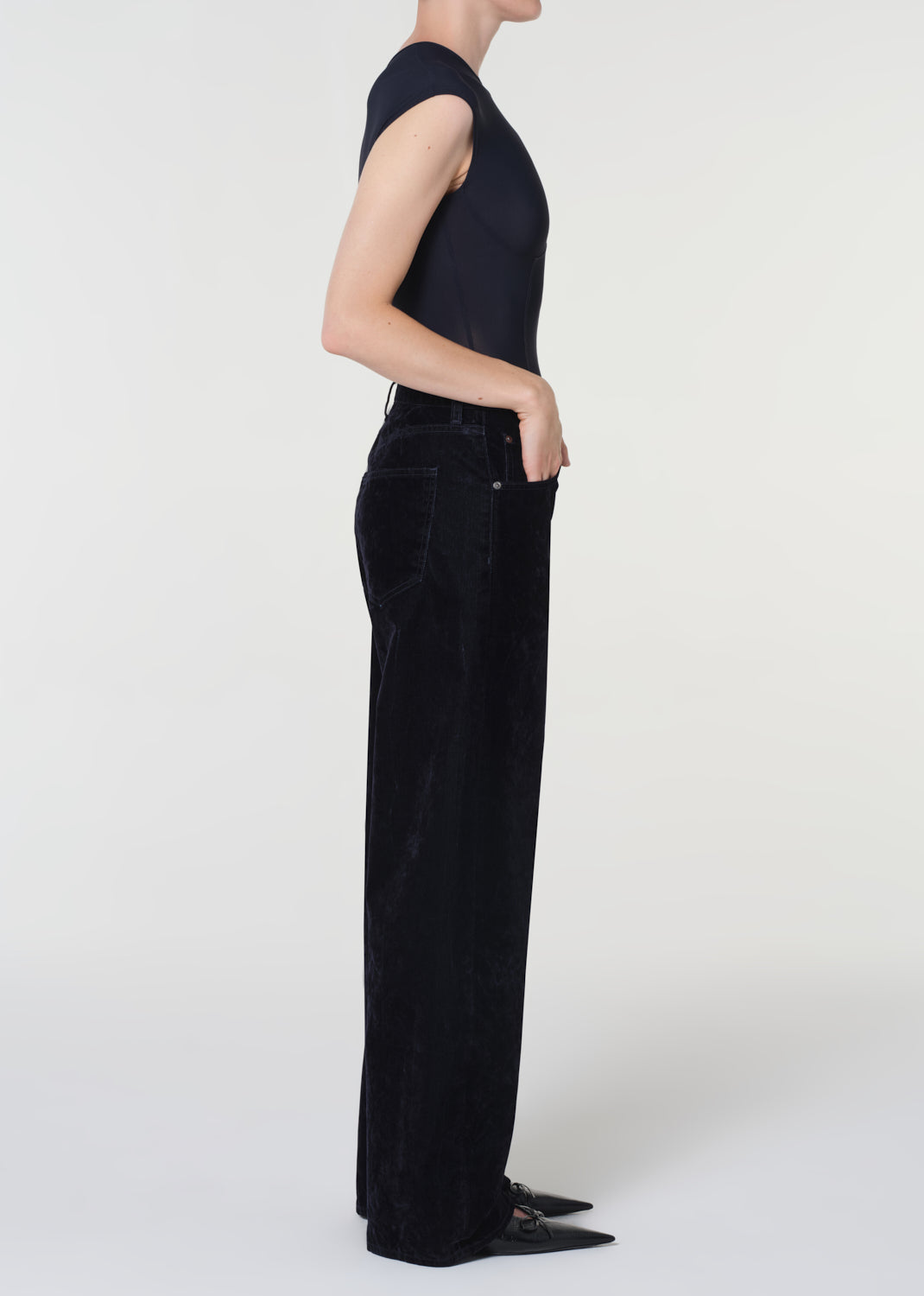 Person wearing black sleeveless top and wide-leg jeans on a white background