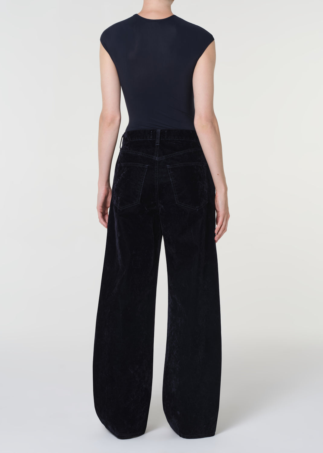 Person wearing a black sleeveless top and wide-leg pants on a white background