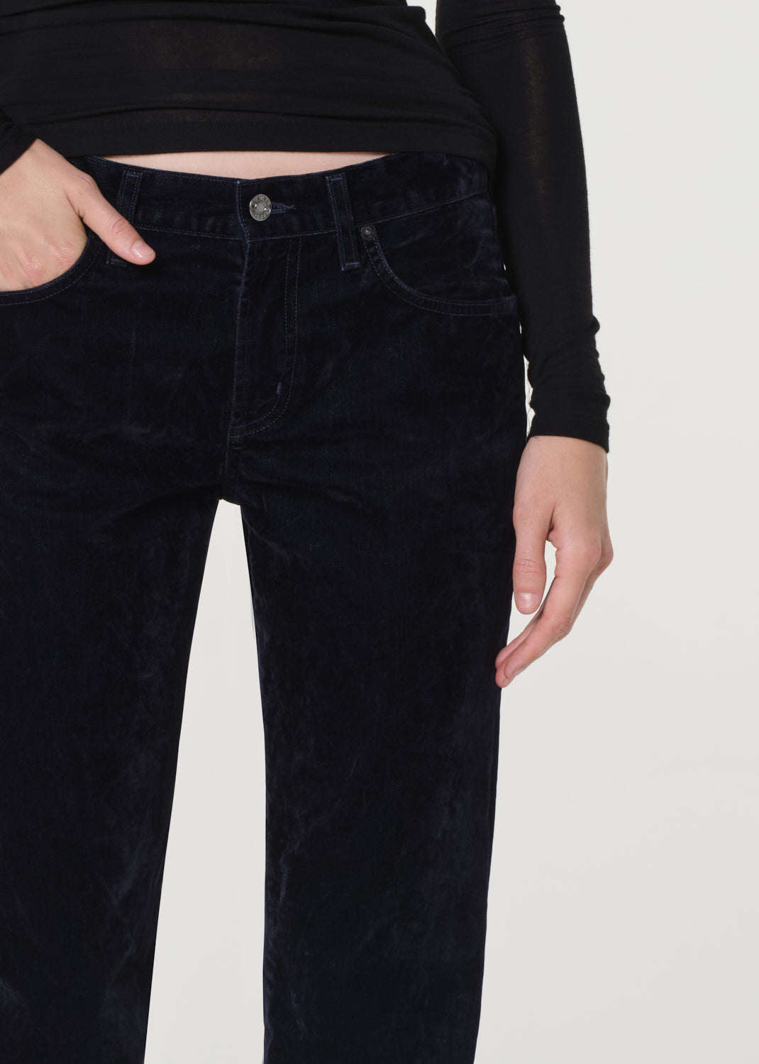 Person wearing a black long-sleeve top and blue velvet pants on a white background
