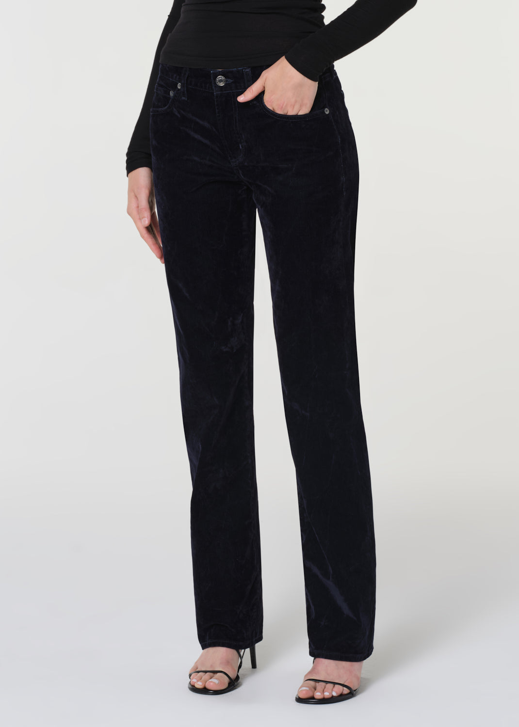 Person wearing a black long-sleeve top and blue velvet pants on a white background