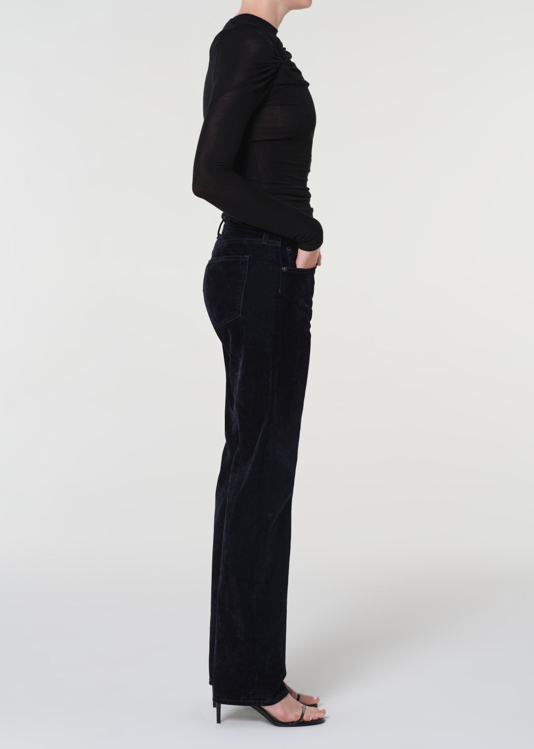 Person wearing a black long-sleeve top and blue velvet pants on a white background
