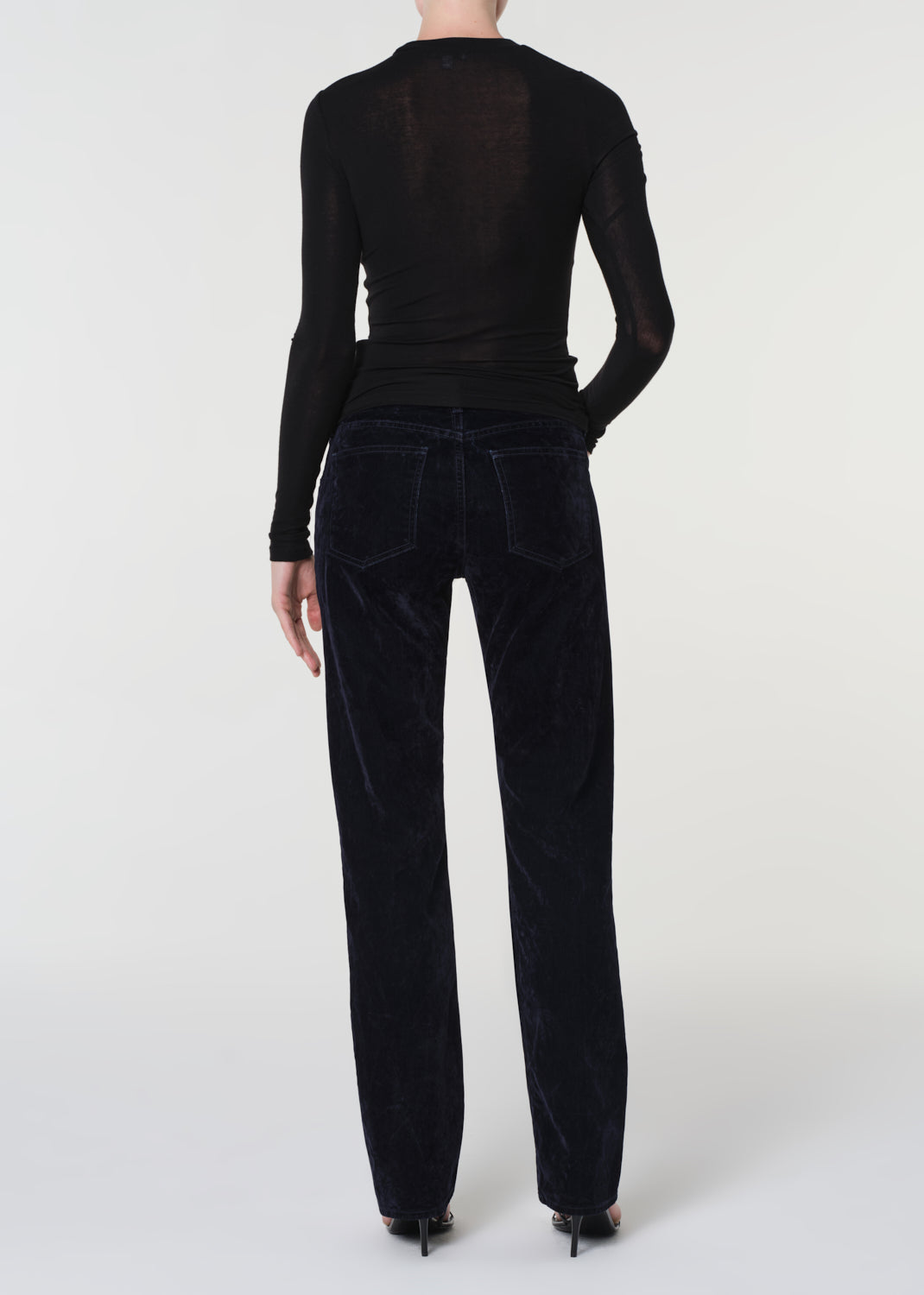 Person wearing a black long-sleeve top and blue velvet pants on a white background