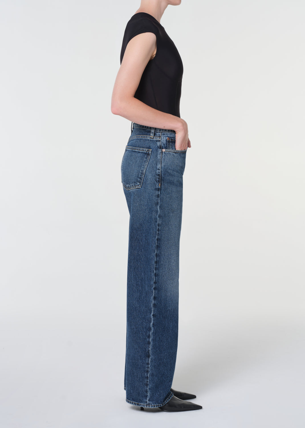 Person wearing blue jeans and a black top on a white background