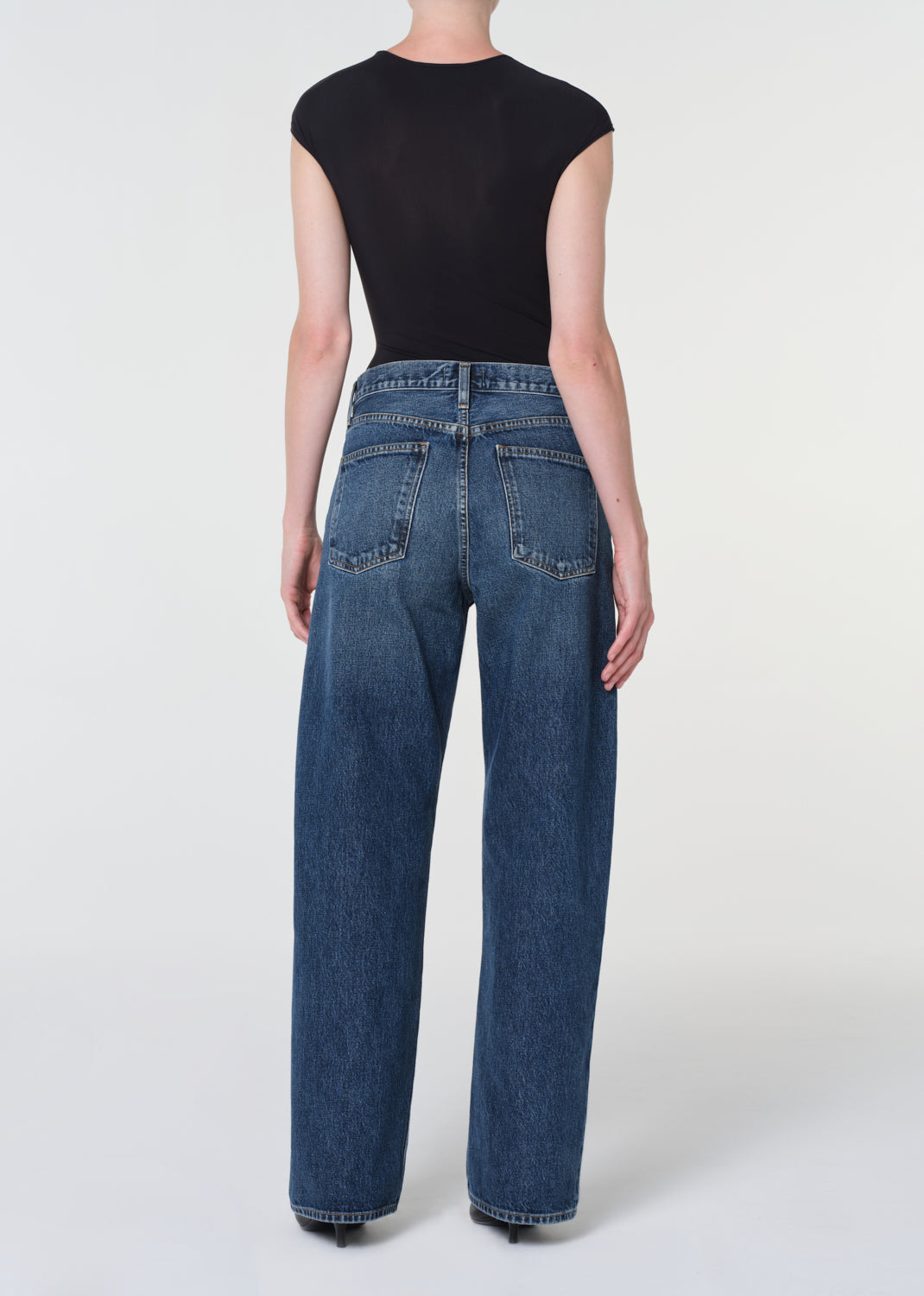 Person wearing blue jeans and a black top on a white background