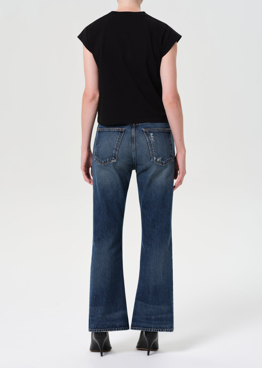 Person wearing blue jeans and a black top on a white background