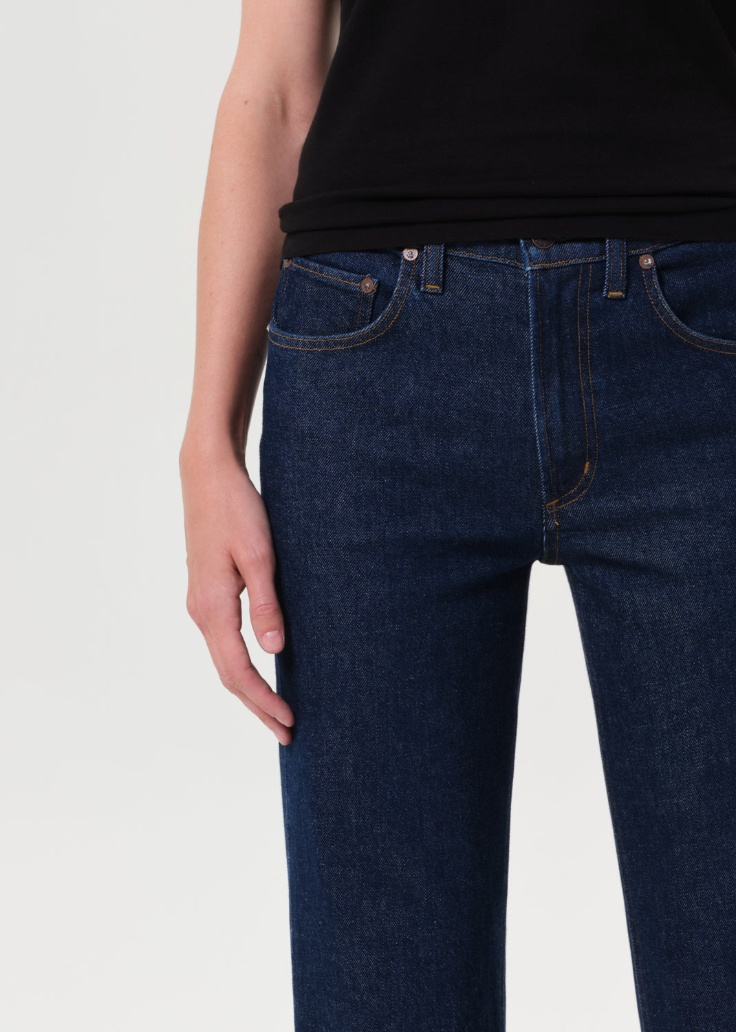 Person wearing dark blue jeans and a black top on a light gray background