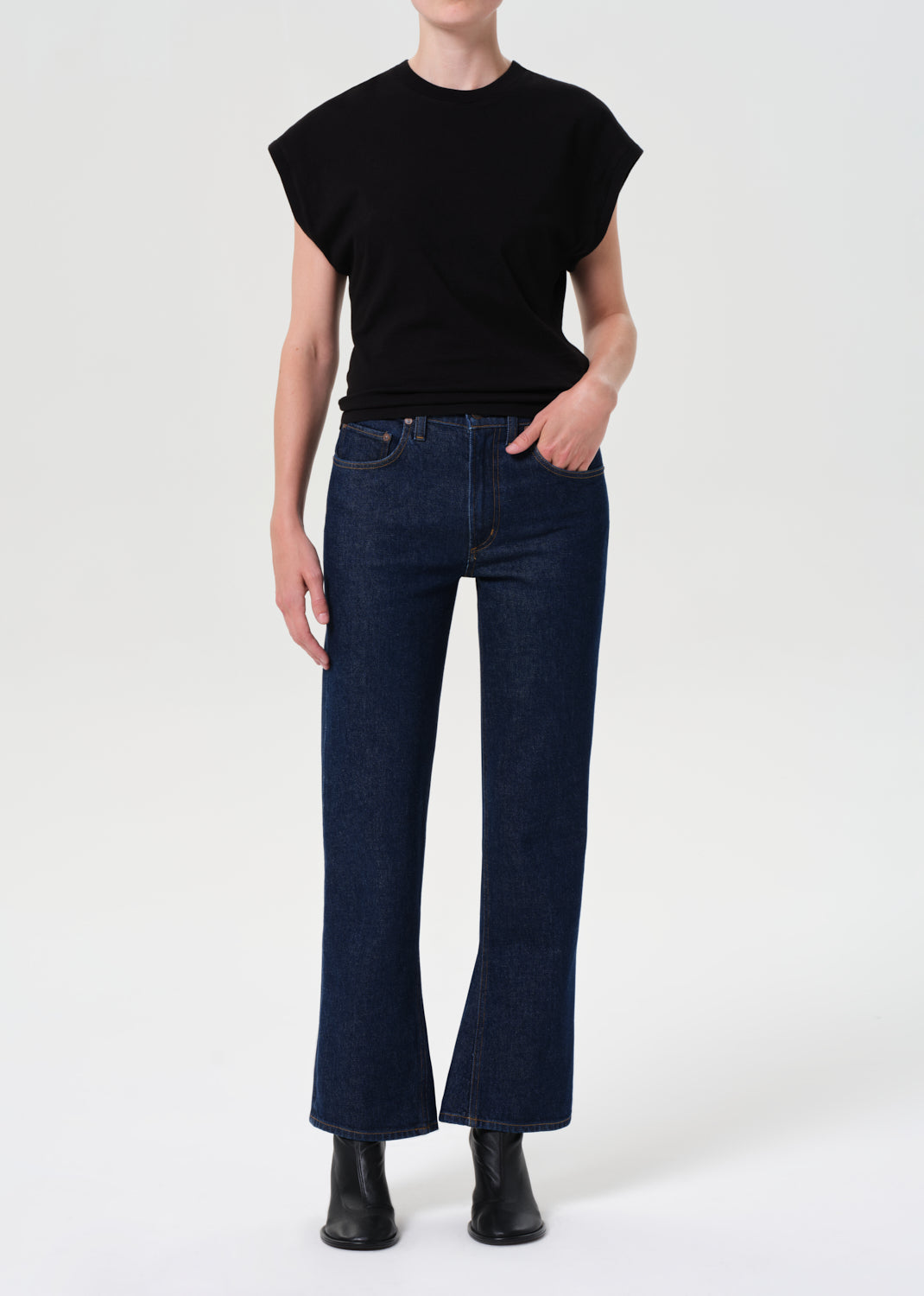 Person wearing a black sleeveless top and dark blue jeans on a white background