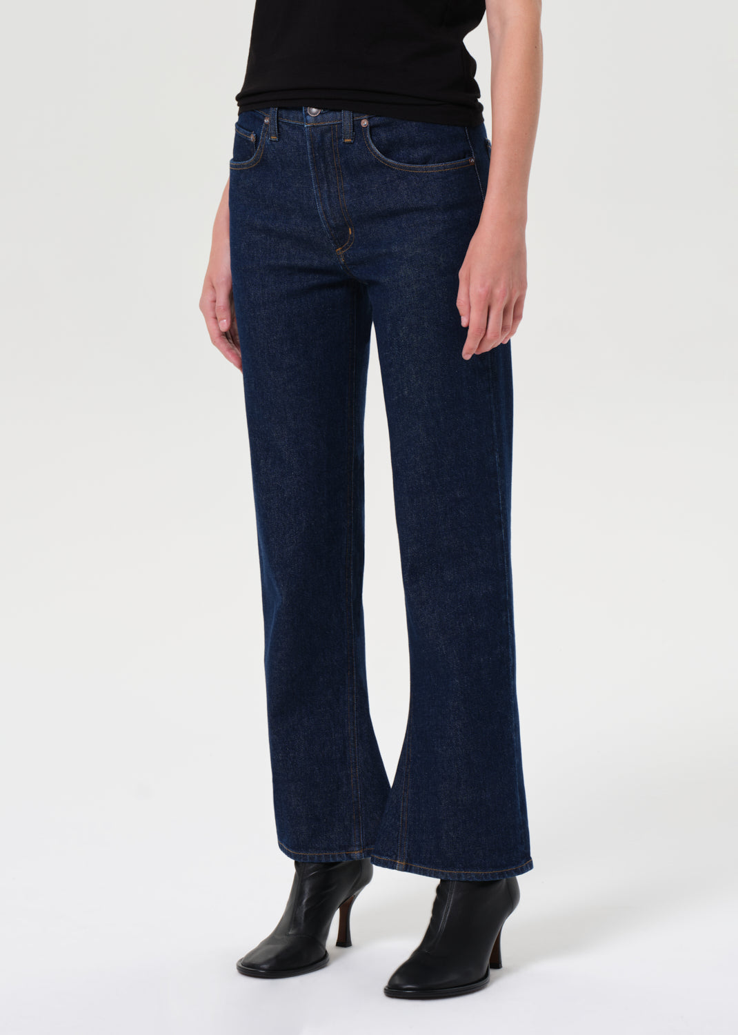 Person wearing dark blue jeans and black boots on a white background